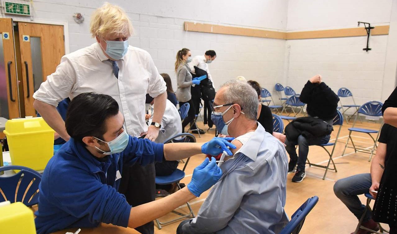 The Prime Minister of the United Kingdom, Johnson, is standing and watch a people who receiving covid-19 vaccine